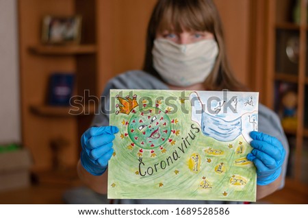 Hands in protective gloves hold a drawing of a coronavirus. A woman on a self-isolation demonstrates a thematic drawing. Shooting indoors. A real man. Blurred background.