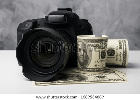 A black digital camera and banknotes on a white table with grunge background.