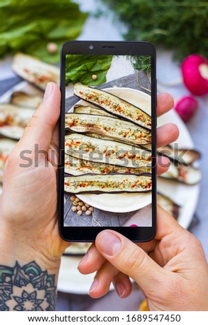 Phone picture of food. Hands make smartphone photography of grilled eggplants for social media blogging. Concept for online order services. Vegan meal.