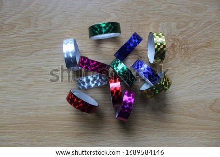 Various colored ribbon stickers stacked together on a wooden floor with light and shining through.