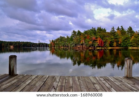 A Day At the Lake. Dock overlooking a lake with an island ablaze in autumn color. Ludington State Park. Ludington, Michigan. Royalty-Free Stock Photo #168960008