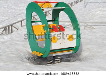 Children's swing in the form of a car on the playground against the background of winter snowdrifts. Concept of children's entertainment and street games. Stock photo for web and print with empty