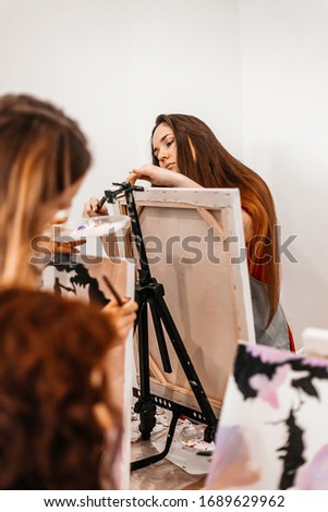 A young woman painstakingly draws her picture with brushes on easels in an art class. learning to draw , art school, creativity and the concept of people