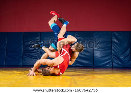 Two strong wrestlers in blue and red wrestling tights are wrestlng  on a wrestling carpet in the gym. Young man doing grapple.