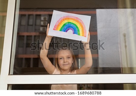 Kid painting rainbow during Covid-19 quarantine at home. Girl near window. Stay at home Social media campaign for coronavirus prevention, let's all be well, hope during coronavirus pandemic concept Royalty-Free Stock Photo #1689680788