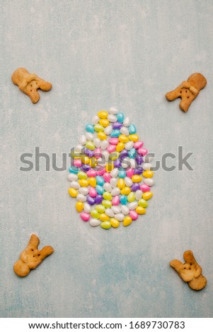 Easter egg emblem made of colored candies on a blue background with cookies and confetti