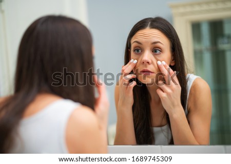 Tired woman looking at her eye bags in the bathroom. Royalty-Free Stock Photo #1689745309