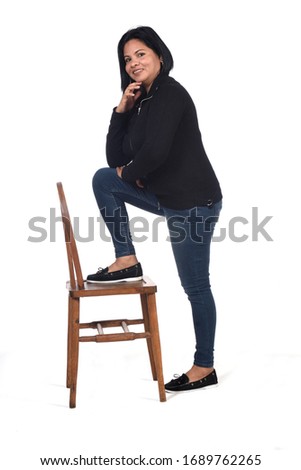 woman playing with a chair in white background, hand on chin and foot on the chair
