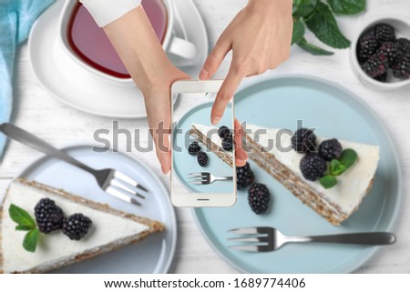 Food blogger taking picture of delicious cake with berries at white wooden table, closeup
