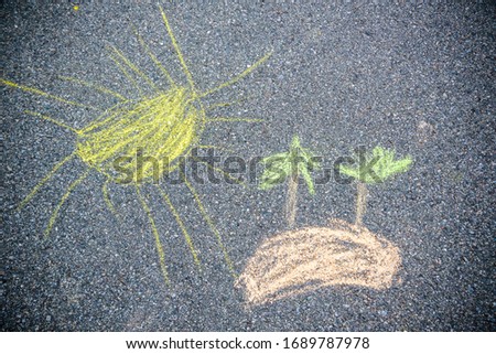 Closeup top view of child's chalk drawing of tropical beach. Blue sea water, yellow sun, sandy island with green palms growing painted at sidewalk outdoors at city park. Horizontal color photo.