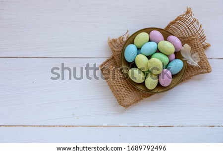 Still life photo of speckled candy covered chocolate easter eggs in a brass bowl on a white wooden background.