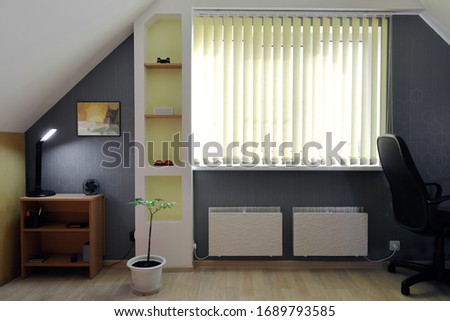 Cozy interior of the attic living room in contrasting tones of dark and white with a wallpaper pattern and a picture on the wall. Sunlight penetrates through the window through the blinds