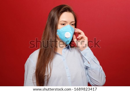 coronavirus pandemic, close-up portrait of young woman on red background in protective medical mask,