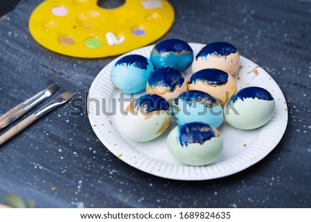 dark background, white dish, a lot of eggs on it, brushes for painting, holiday, Easter.