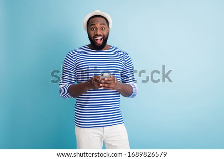 I see ocean! Photo of funny dark skin guy traveler good mood hold telephone app chatting friends wear white sun cap striped sailor shirt shorts isolated blue color background
