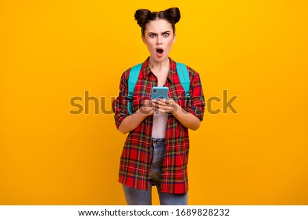 Photo of beautiful shocked student lady hold telephone read email exam bad results walk college open mouth wear blue bag casual plaid shirt jeans isolated yellow color background