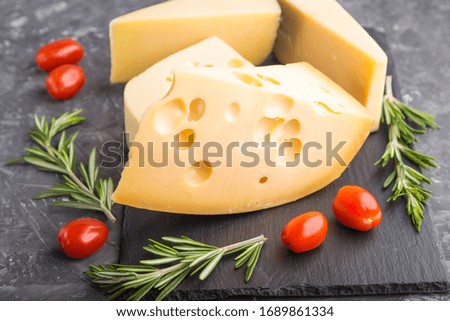 Various types of cheese with rosemary and tomatoes on black slate board on a black concrete background. Side view, close up, selective focus.