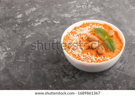 Carrot cream soup with sesame seeds and almonds in white bowl on a black concrete background. side view, close up, copy space.