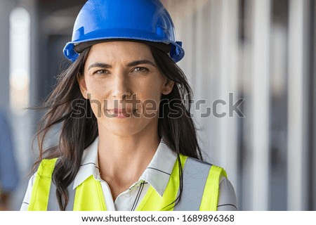 Portrait of successful woman constructor wearing helmet and safety yellow vest. Portrait of architect standing at building site and looking at camera with copy space. Mature successful woman engineer. Royalty-Free Stock Photo #1689896368