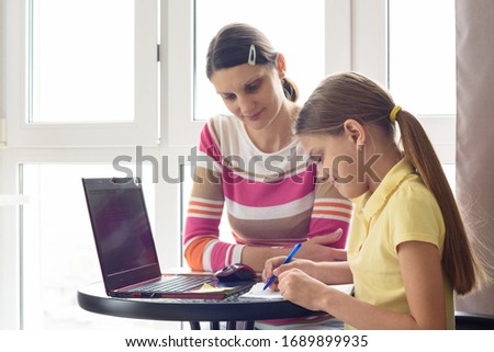 A tutor teaches a child at home, a girl writes in a notebook