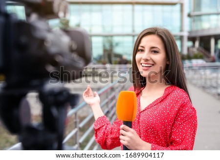 Young female journalist with microphone working on city street Royalty-Free Stock Photo #1689904117
