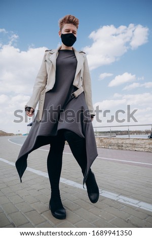a girl with short hair walks down the street in a black antiviral mask