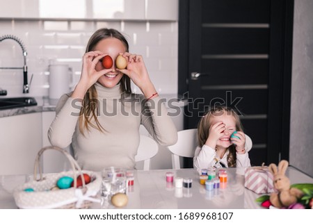 A mother and her daughter painting Easter eggs. Happy family preparing for Easter.