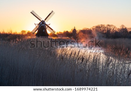 Dutch sunrise with a traditional windmill at a small river in the spring fog.