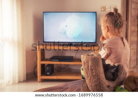 Child watching cartoon on tv in house during self-isolating with warm light from window and rear view as unrecognizable person