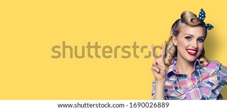 Pin up girl. Excited happy adorable woman showing two fingers or victory gesture hand sign. Retro fashion and vintage picture. Yellow background. Copy space for some slogan, imaginary or text. 