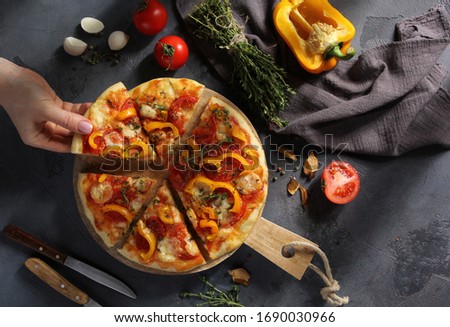 Italian cuisine. Pizza with mozzarella, yellow peppers, tomatoes and thyme on a wooden board on a grey background. Vegetable pizza with hands. Rustic. Background image, copy space