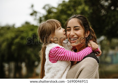 Girl kissing on the cheek of her nanny at the park. Babysitter having fun with a girl at the park. Royalty-Free Stock Photo #1690046911
