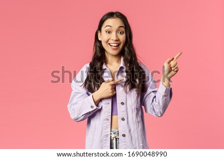 Portrait of enthusiastic young girl found excellent online courses to subscribe during quarantine, pointing fingers right asking friend join together, smiling amused, pink background