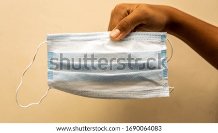 Hand holding a 3 layer surgical mask on a clear background.