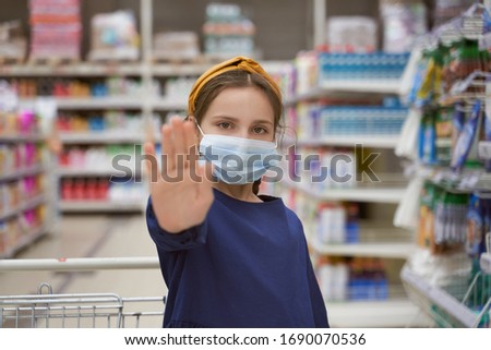 Girl in medical mask reaches hand and shows stop sign shopping in supermarket during outbreak coronavirus pneumonia makes panic stock products. Empty store shelves set things quarantine self-isolation
