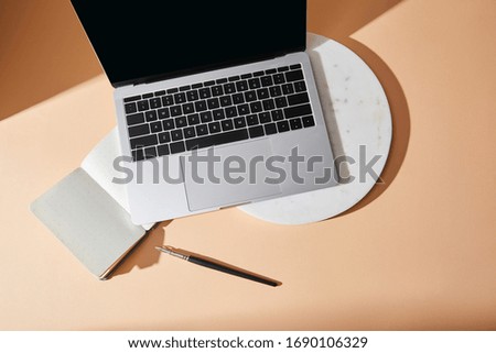 top view of laptop on marble board, copybook and paintbrush on beige background