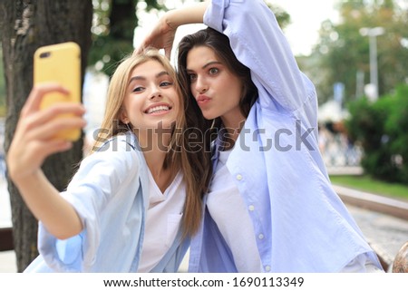 Two laughing friends enjoying weekend together and making selfie on city background.