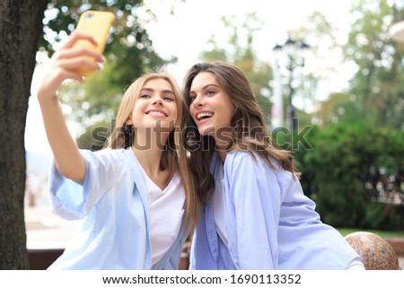 Two laughing friends enjoying weekend together and making selfie on city background.