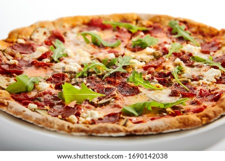 Pepperoni pizza slices with arugula on plate. Traditional italian cuisine, delicious fast food. Savory dish with salami and cheese on white background. Tasty pizzeria meal on plate
