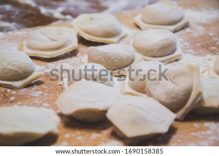 Close up picture of home made dumplings with meat on wooden background with traditional processing of cooking with raw products as preparation of dish to eat it all together with family, food concept