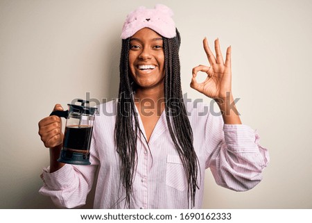 Young african american woman wearing pajama making coffee tired at night doing ok sign with fingers, excellent symbol