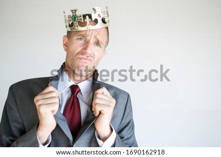 Cocky businessman wearing golden jeweled crown popping his collar with an arrogant expression Royalty-Free Stock Photo #1690162918