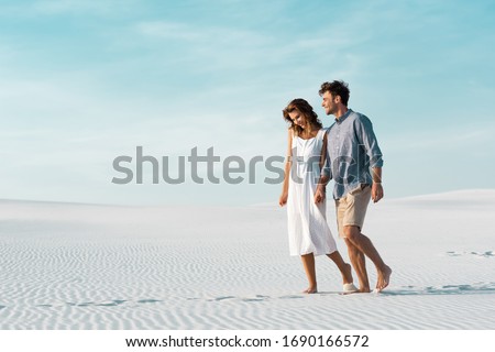 young couple walking on sandy beach against blue sky Royalty-Free Stock Photo #1690166572
