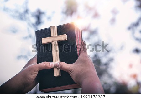 Hands raised the Bible with cross in hands of human, Christian concept background.