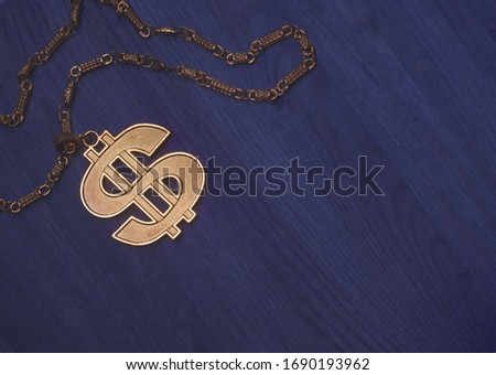Golden necklace with the dollar logo on a blue wooden table with copyspace