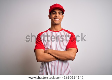 Young handsome african american sportsman wearing striped baseball t-shirt and cap happy face smiling with crossed arms looking at the camera. Positive person.