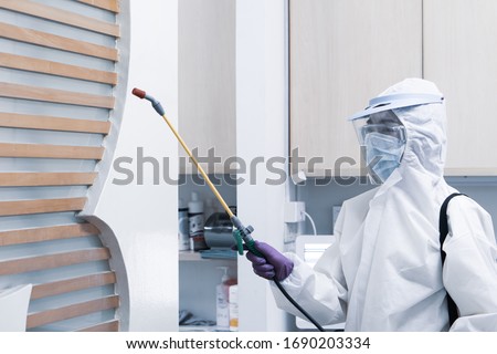 worker from decontamination services wearing personal protective equipment or ppe including white suit mask and face shield spraying disinfectant to cleaning coronavirus infection Royalty-Free Stock Photo #1690203334