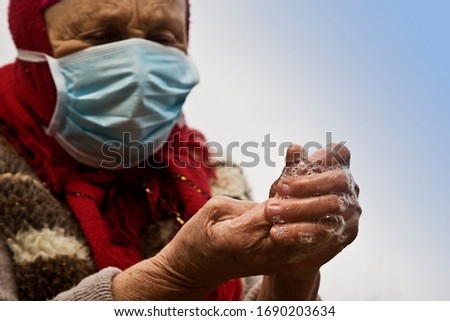 An elderly woman in a medical mask treats her hands with a disinfectant to prevent infection with a cornavirus infection. A large number of people infected with coronavirus in the United States. Royalty-Free Stock Photo #1690203634