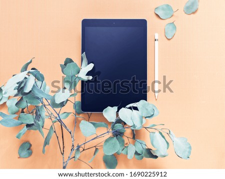 The concept of working on a tablet for illustrators, freelancers, home use. An electronic tablet, a stylus and a branch of a eucalyptus are on a cardboard background. Flat lay. Copy space.