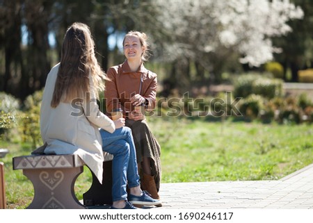 Two attractive girls are talking in the Park, smiling and laughing. Concept of takeaway coffee, natural beauty, communication. Copy space. Royalty-Free Stock Photo #1690246117